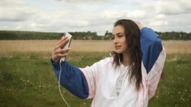 Gölün arkasındaki parkta güzel mutlu bir kız selfie çeker ve kulaklıkla müzik dinler.