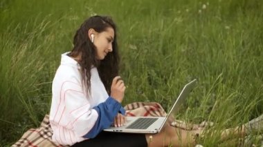 25 yaşında esmer bir kadın dizüstü bilgisayarla doğada yatıyor ve internette çalışıyor.