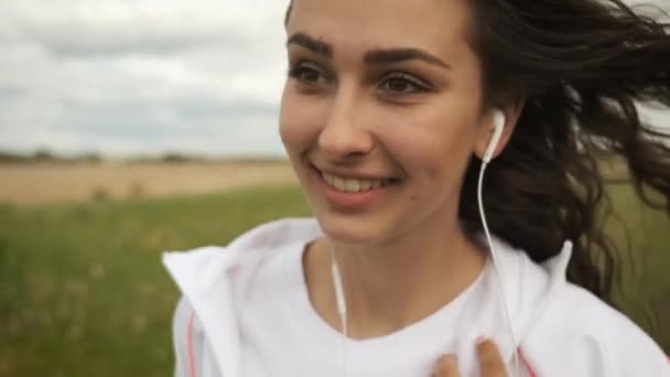 Belle fille d'apparence caucasienne marche dans le parc regarde le téléphone et écoute de la musique sur écouteurs — Video