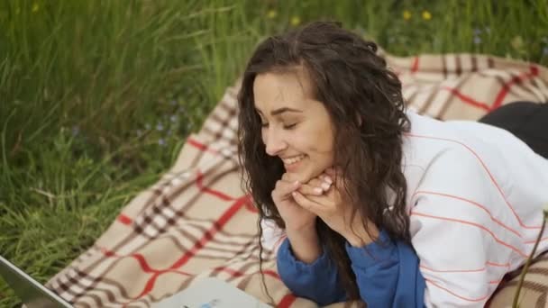 Vrolijk mooi aziatisch meisje liggend in de natuur en praten op video gesprek met vrienden — Stockvideo