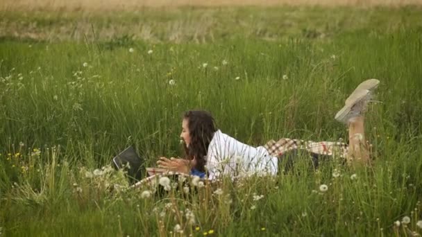Brunette vrouw 25 jaar oud liggend in de natuur met laptop en werken online — Stockvideo