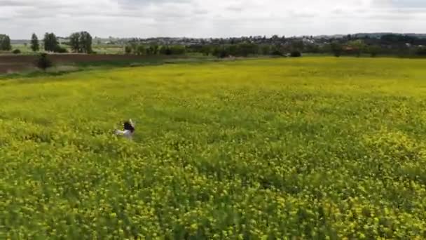 Lycklig kvinna som springer på ett blommande gult och grönt fält. Vårvåldtäkt. Drönarflygning över vacker natur. Landskap i Europa — Stockvideo