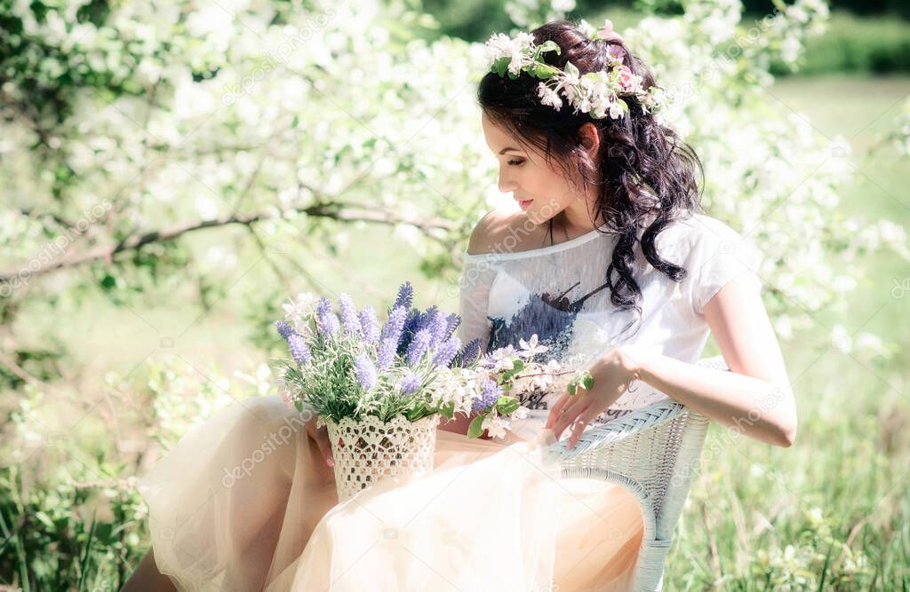 A romantic cute girl with a wreath and a bouquet of lilac is sitting in a chair against the background of green nature on a sunny day. Album cover
