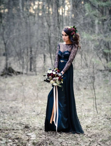 A Gothic woman in a black dress with a bouquet of flowers in a mysterious forest. Black magic, Gothic beauty, mystical image. Halloween, black widow