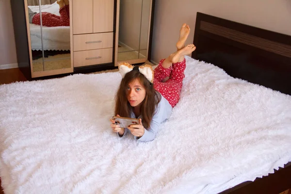 Удивлённая Девушка Лежит Белой Кровати Держит Руках Телефон — стоковое фото