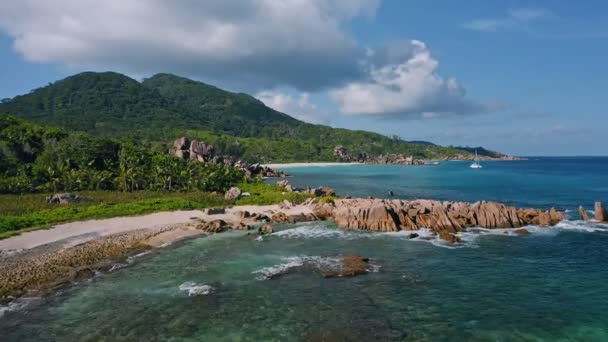 images aériennes de drones du littoral tropical avec des roches de granit et des vagues océaniques roulant contre le rivage yacht catamaran solitaire amarré dans la lagune de la grande anse la digue île seychelles 