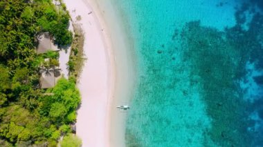 Palmiye ağaçlarıyla kaplı helikopter adasındaki tropik plajın hava görüntüleri. Mavi lagün masmavi su ve mercan resifleri. Beyaz kumsalda yalnız bir turist teknesi.