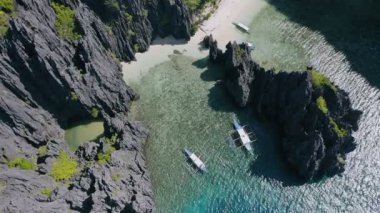 Miniloc Adası El Nido Palawan Filipinleri 'ndeki gizli lagün sahilindeki engebeli karst kayalıkları arasında demirlemiş turist teknelerinin havadan aşağı daire görüntüsü.