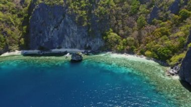 Filipinli teknelerin mavi gölde mercan resiflerinin tepesinde yüzüşünün hava görüntüsü. Büyük kayalıkların önünde. El Nido Palawan Filipinleri.