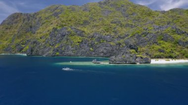 El Nido Palawan Phillippines 'deki matinloc adasının yakınındaki hava manzaralı turnuva mavi sularda kayık, engebeli kireçtaşı dağları ve arka planda gözlerden uzak plajlar.
