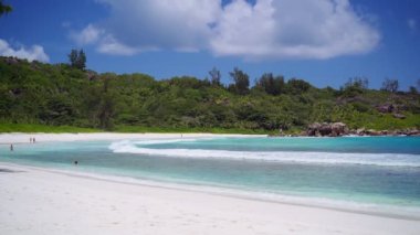 La Digue Seyşeller 'deki Anse Coco Plajı. Bilinmeyen turist sığ mavi okyanus gölünde yüzüyor. Sakin dalgalar beyaz kumsala yuvarlanıyor.