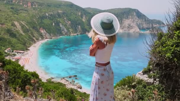 希腊岛屿金发碧眼的美女 头戴礼帽 面容迷人 面对着令人叹为观止的牡丹湾夏季度假生活方式探险无忧无虑的快乐与幸福理念 — 图库视频影像