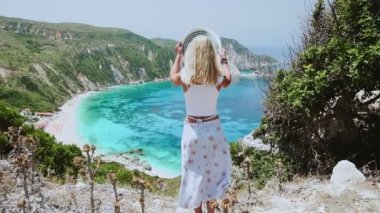 Yaz tatili mutlu genç kadın turkuaz bir körfezin önünde güneş şapkasını takıyor ve deniz hanımına bakıyor Yunan yaz tatili yaşam tarzı konseptinin tadını çıkarıyor.