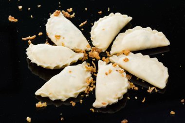 Siyah bir zemin üzerinde yarı bitmiş mantalar soğanlı bir çemberin içinde yatıyor.