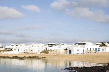 Arka planda kasaba olan kumlu bir sahil.