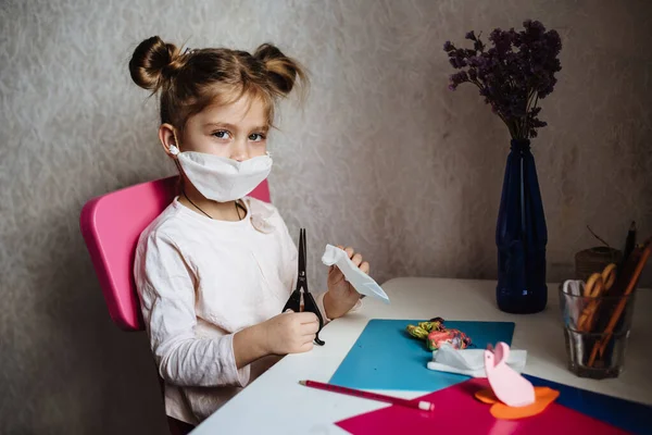 Tıbbi maskeli beş yaşındaki kız yaratıcı bir işte çalışıyor. Kendi elleriyle koruyucu maske takıyorlar. Bir çocuğu karantinaya almak için ne yapılır? Karantina sırasında evde eğitim. Evde kalıp eğlenin..