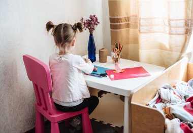 Kız evde, anaokulunda yaratıcılıkla meşgul. Çocuk kağıttan kesiyor. Çocuk sanatı. El işi konsepti. El yapımı. Çocuğun erken gelişimi. Bir çocuğu karantinaya almak için ne yapmalı?