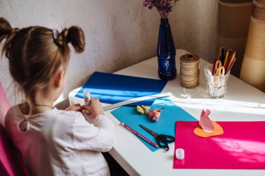 Kız evde, anaokulunda yaratıcılıkla meşgul. Çocuk kağıttan kesiyor. Çocuk sanatı. El işi konsepti. El yapımı. Çocuğun erken gelişimi. Bir çocuğu karantinaya almak için ne yapmalı?