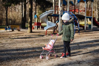 Kapalı oyun alanının arka planında koruyucu maskeli üzgün küçük kız. Tıbbi maskeli bir çocuk parkta yürüyor. COVID-19 'a karşı karantina önlemleri. Koronavirüs salgını.