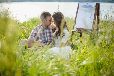 Güzel bir çift nehir ve yeşil doğanın arka planında sarılıp öpüşüyor. Aşk hikayesi. Kız dışarıda erkek arkadaşını öpüyor..