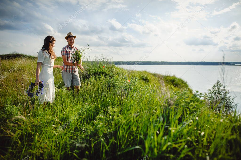 Loving couple man and woman collect wildflowers by the river on a sunny day. Love story.