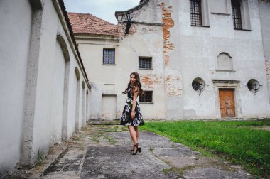Elbiseli güzel esmer, eski kalenin avlusuna gider. Gri vintage binanın arka planında siyah elbiseli şık bir kız. Büyük üzgün gözler..