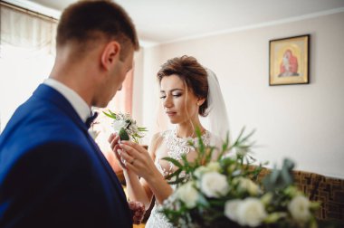 Güzel gelin, gelinin mavi ceketine bir yaka çiçeği iliştirir..