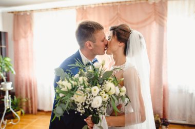 Gelin ve damat ellerinde düğün buketiyle öpüşüyorlar. Düğün töreni. Gelinle damadı öp. Film tahılı