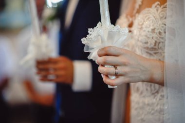 Gelin kilisedeki bir nikah töreninde mum tutuyor, yakın çekim. Gelinin parmağında altın alyans