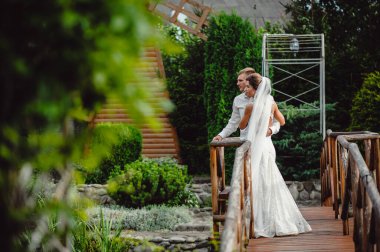 Şık bir damat ve güzel bir gelin düğün günü eski ahşap köprüde duruyor. Parktaki düğün töreninde aşık genç bir çift.