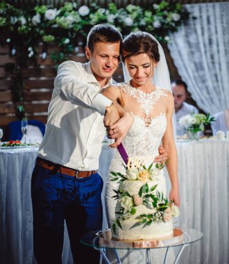 Gelin ve damat düğün yemeğinde düğün pastalarını kesiyorlar. Eller narin pembe çiçeklerle pastayı keser. Modaya uygun bir pasta. Film sesi