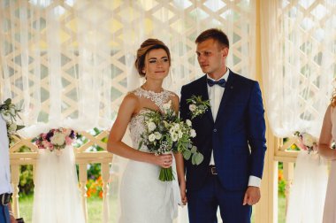 Düğün törenindeki sevgili gelinlerin portresi. Güzel gelin elinde bir buket beyaz çiçek, yeşillik ve smokinli şık bir nişanlı tutuyor..