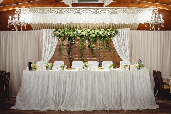 Festive table, arch, stands decorated with composition of white flowers and greenery, candles in the banquet hall. Table newlyweds in the banquet area on wedding party.