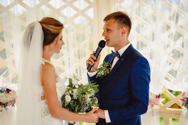 Attractive stylish groom saying a oath, while looking at the stunning bride during wedding ceremony. Sincere speech of the groom at the wedding ceremony. Exchange of wedding vows at the ceremony.