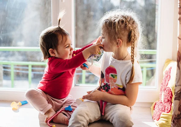 Teaching your child preventive measures against covid-19, viruses and flu. The girl in a protective mask is playing with her sister at the doctor. Care for loved ones. Basic hygiene rules. Pandemia.