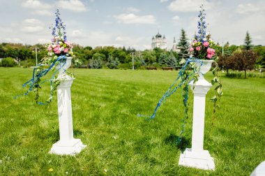 Parkta renkli çiçekli iki kolon duruyor. Düğün kemeri açık havada çiçekler ve sütunlarla süslenir. Düğün dekoru. Fotoğraf Bölgesi