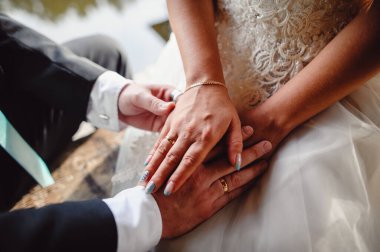 Beyaz gelinlikli gelin ve siyah smokinli damat el ele tutuşun, yaklaşın. Birbirlerinin elini tutan evli bir çiftin parmaklarında altın alyanslar. Düğün töreni.