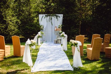 Yeşil ağaçlar ve çimenler üzerinde bir düğün sunağının önünde sandalyeler. Düğün töreni açık havada..