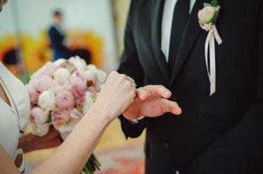 Gelin, nikah töreninde kilisede dururken damadın parmağına bir alyans takıyor. Doğada evlilik töreni. Mücevherler. Yakından. Yeni evliler