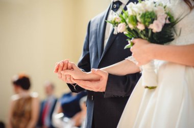 Yakından çekilmiş şık, erkeksi, lüks moda bir fotoğraf ve bir düğün buketi. Gelin ve damat düğün töreninde el ele tutuşuyorlar. Yakın plan. Düğün aksesuarları.