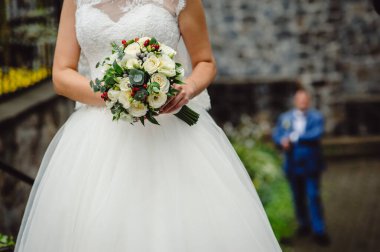 Beyaz gelinlik giymiş gelin elinde beyaz güllerden oluşan şık bir buket tutuyor. Yaklaş. Metin için yer.