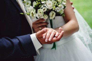 Yakından çekilmiş şık, erkeksi, lüks moda bir fotoğraf ve bir düğün buketi. Gelin ve damat düğün töreninde el ele tutuşuyorlar. Yakın plan. Düğün aksesuarları.
