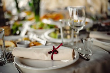 Servis, kurma masası. Tabaklar ve çatal bıçak takımı keten peçeteler kırmızı kurdelelerle süslenmiştir. Kapatın. Restorandaki ziyafet salonunda. Hizmet kavramı. Kutlama. Yıldönümü. Düğün.