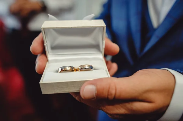 青いタキシードを着た新郎が結婚指輪を手に持っている アップ 新郎の朝 結婚式のアクセサリー 指輪付きの箱を持った男の手 — ストック写真