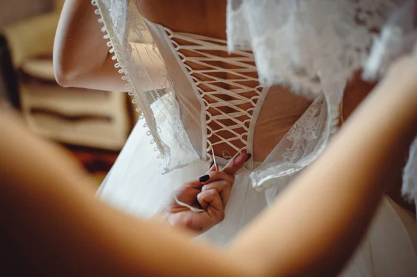 朋友们把紧身胸衣系在新娘的衣服上 伴娘们穿着婚纱 腰围细长 给新娘穿上 — 图库照片