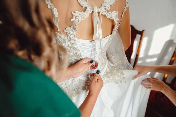 朋友们把紧身胸衣系在新娘的衣服上 伴娘们穿着婚纱 腰围细长 给新娘穿上 — 图库照片