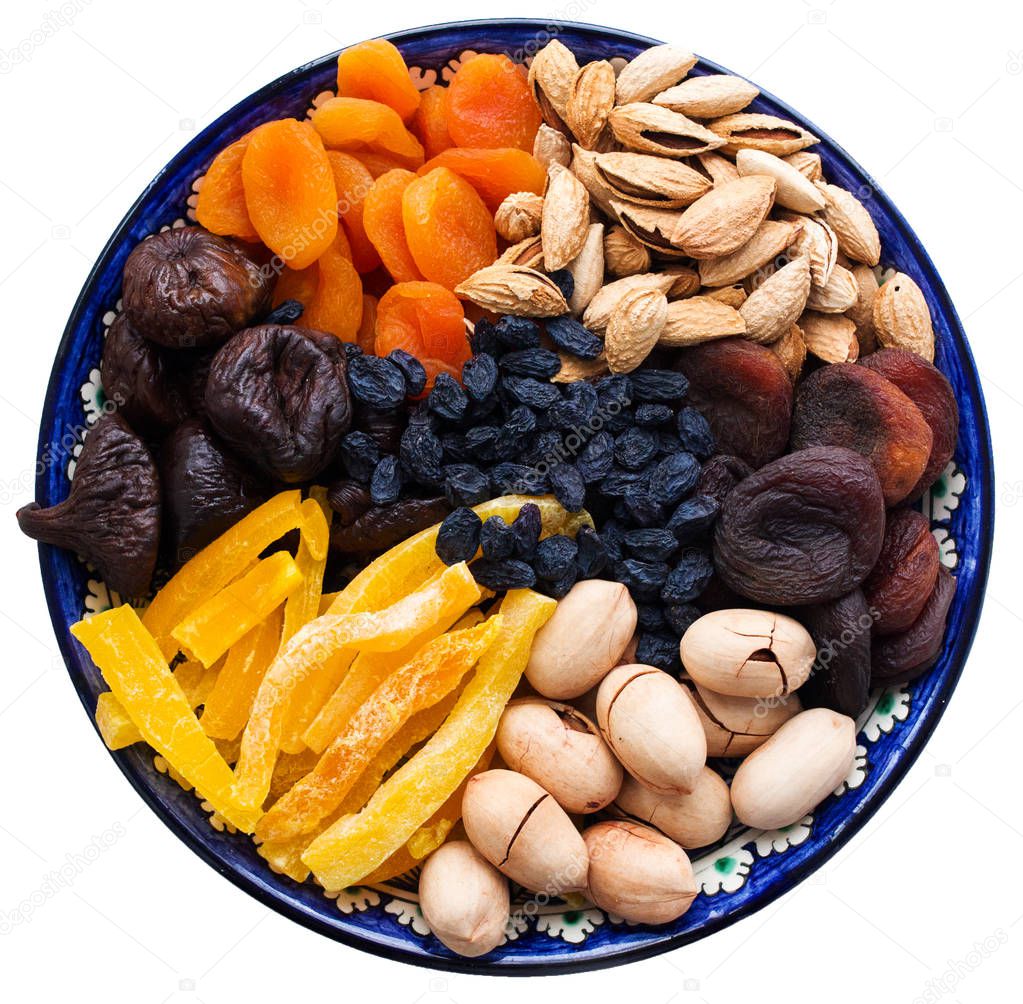 Top view of Central Asian dried fruits and nuts in a typical blue ceramic plate isolated on white background. Dried apricots, mango, figs, raisins, pecan, almond