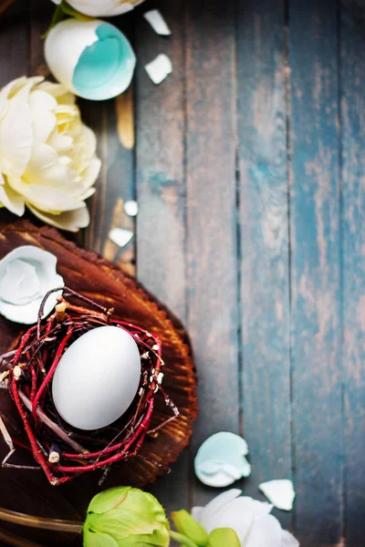 Bílá vejce v malé hnízdečko s světle květinami na dřevěné rustikální pozadí. Velikonoční jarní koncept — Stock fotografie