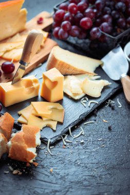 Üzüm, ekmek ve bal ile dekore edilmiş çeşitli peynir, siyah arduvaz kurulu