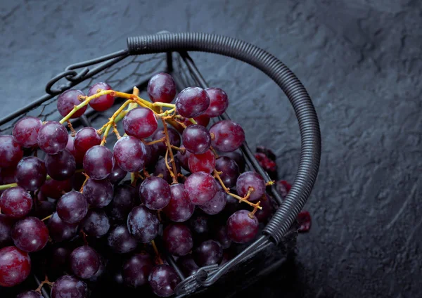 Violet grape bunch in a metal basket on a black slate. Dark mysterious mood